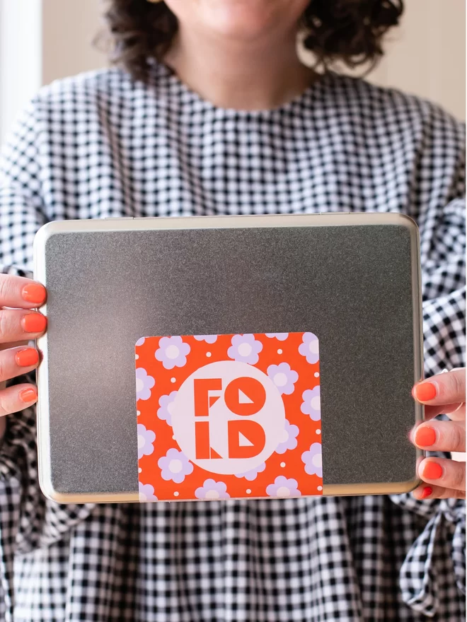 Woman holding a craft tin with FOLD logo & floral design.