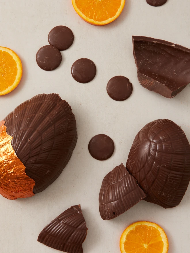 orange milk chocolate easter egg. a chocolate egg photographed partially unwrapped from orange foil with orange slices and chocolate buttons.