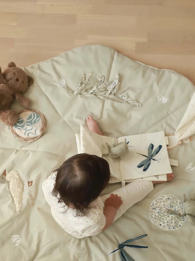 A baby on the activity mat while playing with the fabric book 
