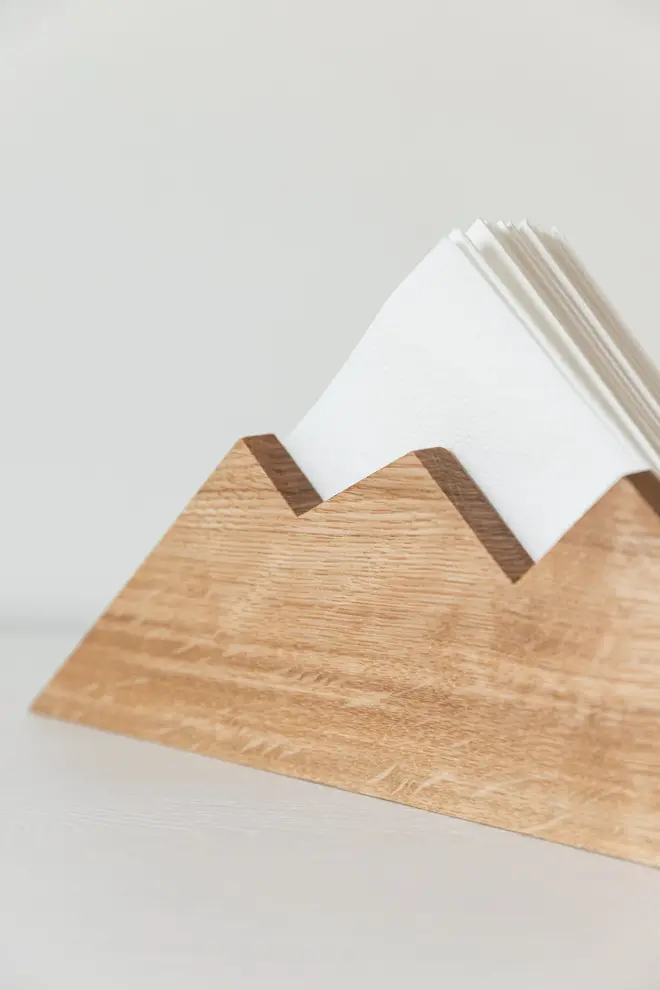 Mountain Napkin Holder, a wooden napkin holder sitting on a plain surface against a white background filled with napkins. 