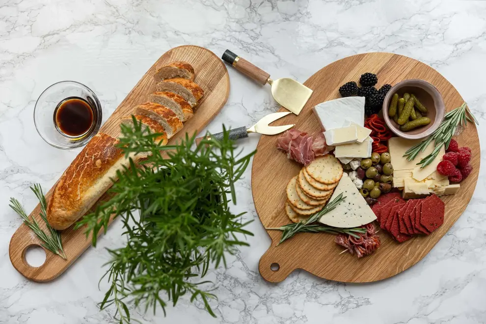 Ash Paddle Serving Board, a wooden serving board sat on a stone surface accompanied by a spread of food. 