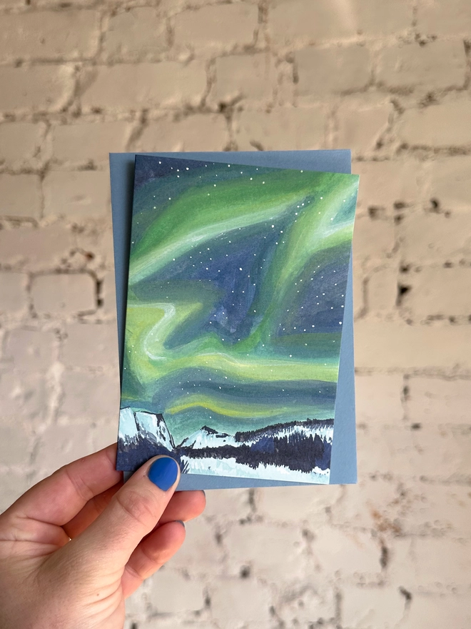 a greetings card featuring an illustration of the northern lights above a snowy landscape with a blue envelope