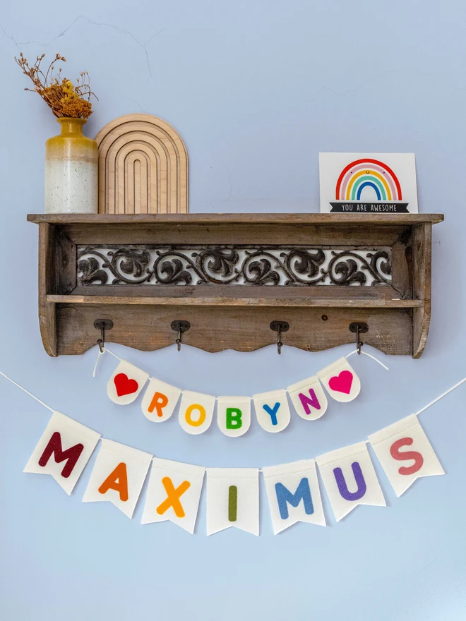 2 lots of Personalised felt name bunting, the bunting is white with rainbow coloured letters. One piece is smaller and bright coloured the other larger and muted colours
