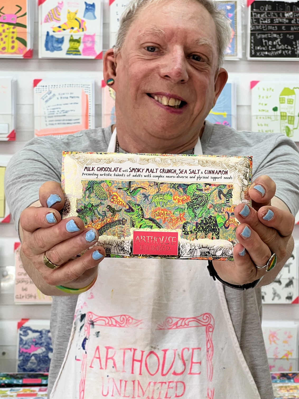 Artist holding charity milk chocolate wrapped in gold foiled card decorated with green dinosaurs 