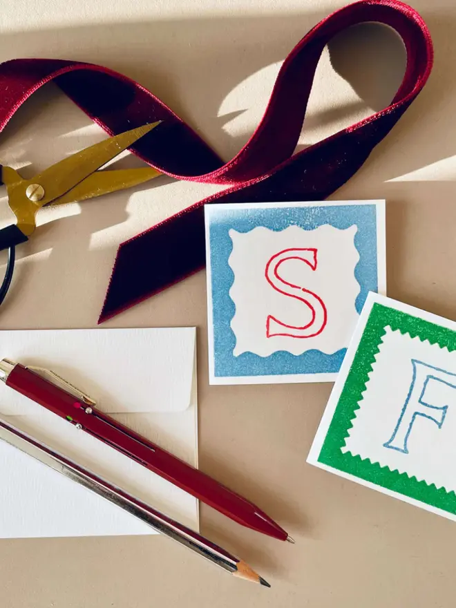 Two hand-printed mini letter cards featuring a red “S” on a blue background and a blue “F” on a green background, each framed with scalloped edges.