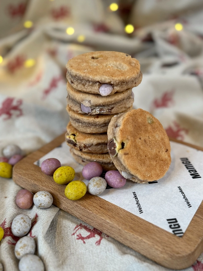 6 Mini Egg Welsh Cakes on a wooden chopping board with a rustic kitchen background and loose mini eggs
