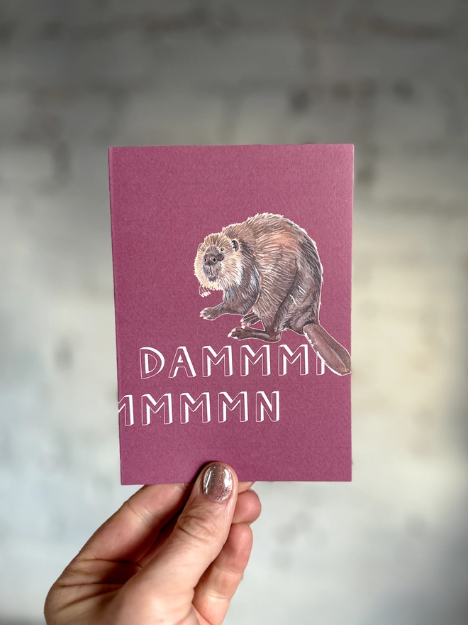 a pinky purple greetings card featuring an illustration of a beaver with the text “dammmmmn”