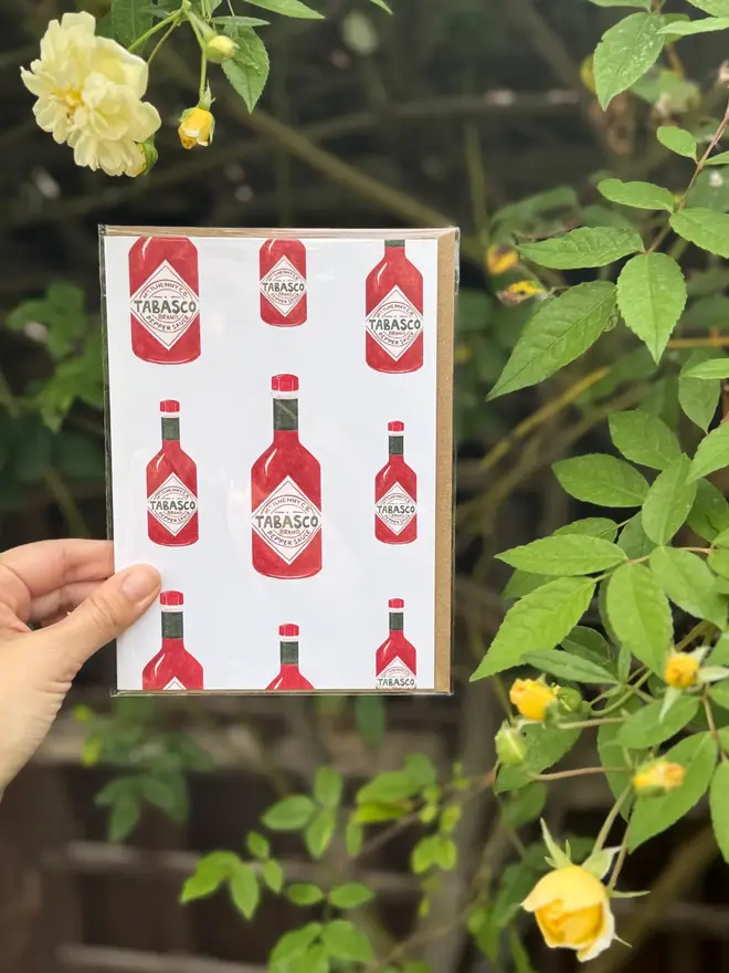 tabasco bottles illustrated card. card photographed against rosebush backdrop.