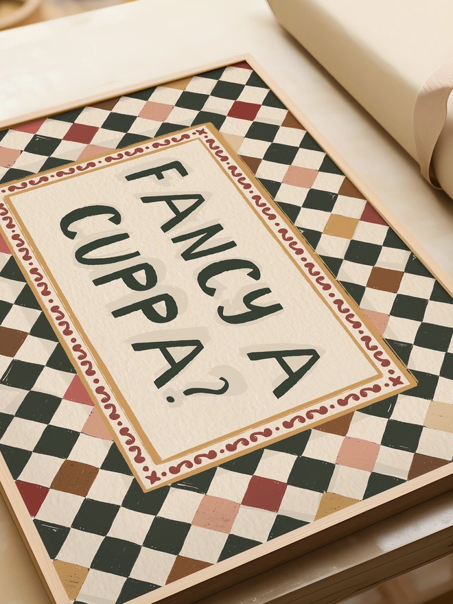 checkerboard framed print with biscuit colour squares with 'fancy a cuppa?' text inside in a hand illustrated style