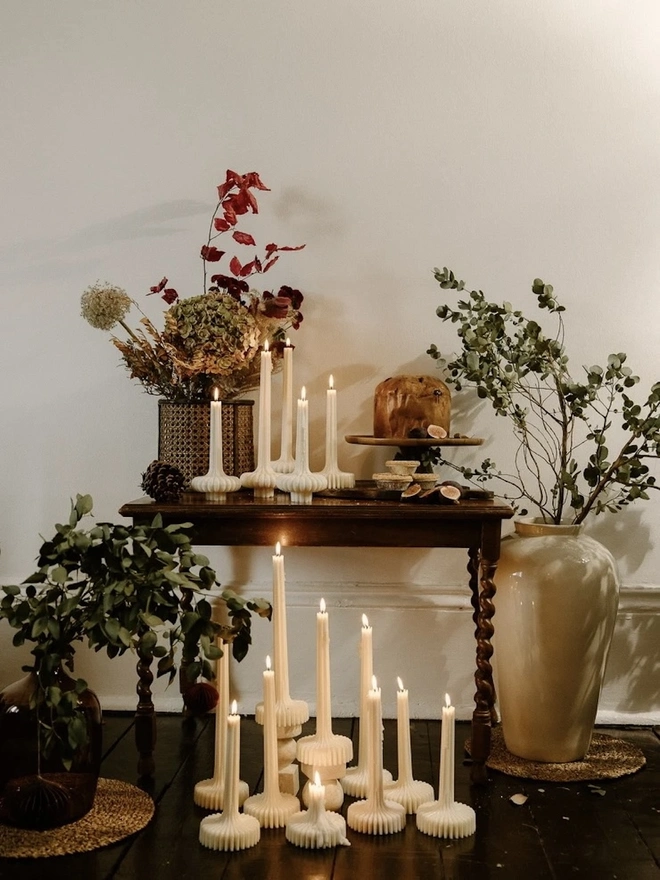 Pair Of White Flair Candles (Set Of 2). A styled corner with lit fluted candles on an antique barley-twist table and gathered on the floor, among dried hydrangeas, eucalyptus, figs and a large cream vase. The candles bring warmth and height to seasonal entertaining spaces.