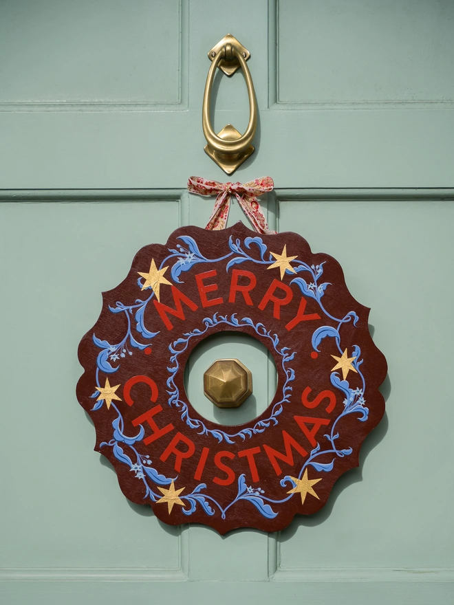Depp Reddish Brown Hand painted Christmas Wreath with red lettering and gold leaf stars on a pale green front door