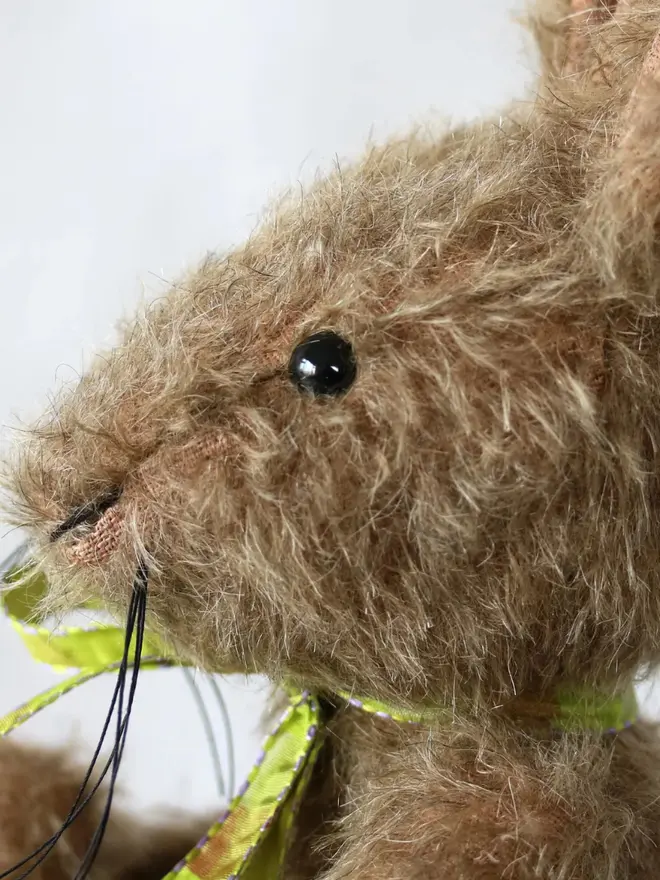 Handmade brown stuffed rabbit with long ears and a green ribbon bow sitting upright against a plain background.