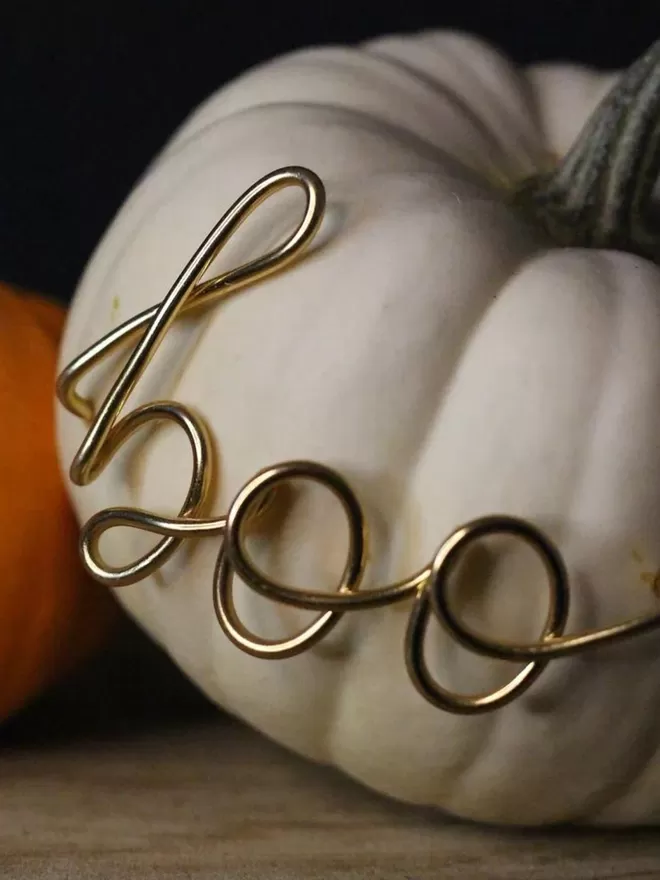 Gold wire mini boo seen stuck into a white pumpkin seen close up.