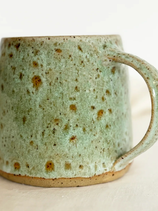 Ceramic Mug. A close-up of a green, speckled rustic mug set against a clean background.