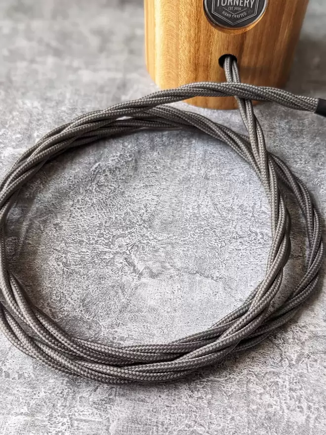 A carefully coiled power cable in twisted elephant grey leading to a UK 3 pin plug in Black.