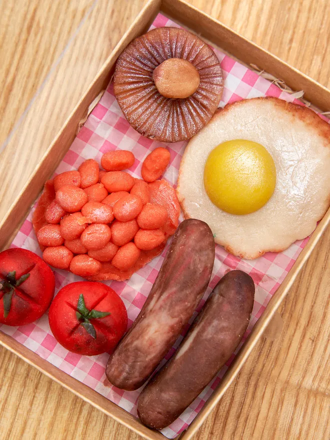 Brekkielicious Marzipan Box, sweet marzipan box displayed on a table surface. In the image are marzipan eggs, beans, mushrooms, tomatoes and sausages along with traditional red and white patterned cloth. 