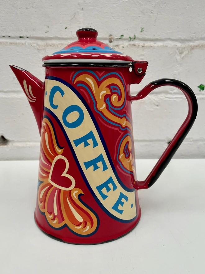 Red vintage coffee pot, hand painted with a fairground inspired design in pink, orange and yellow. 'Coffee' is painted in a banner through the centre of the design.