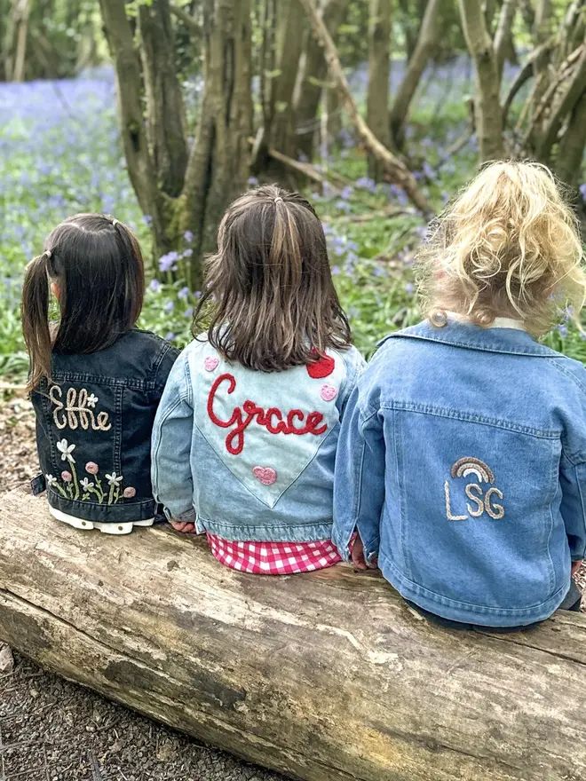 three young girls wearing personalised jackets, facing away from camera