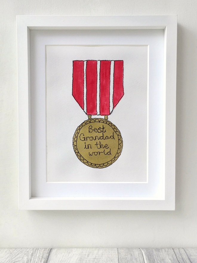 A hand painted gold medal artwork with a red ribbon and an embroidered message reading Best Grandad in the world