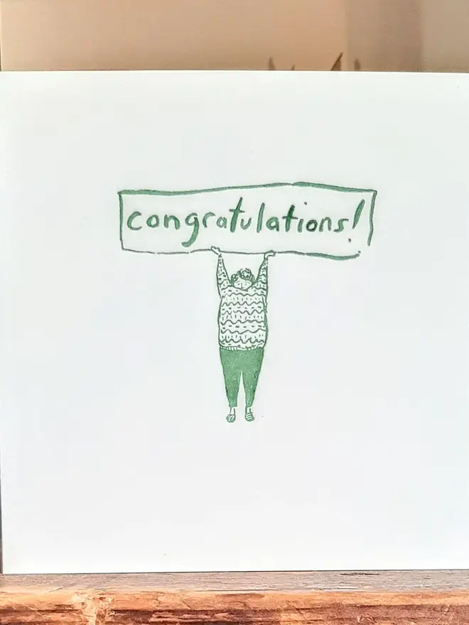 'Congratulations' Letterpress Handprinted Greetings Card, a white congratulations card with a green design against a wooden background. 