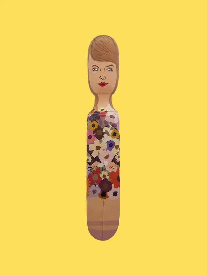 Wooden Door Stopper (Swifty Floral Outfit), a colourful wooden door stop sitting on a yellow surface. 