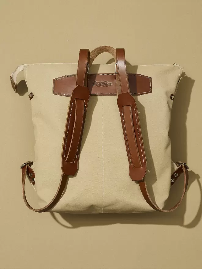 Back view of the taupe zip top Shortwood rucksack with brown leather straps and suede shoulder pads shown on a natural background.