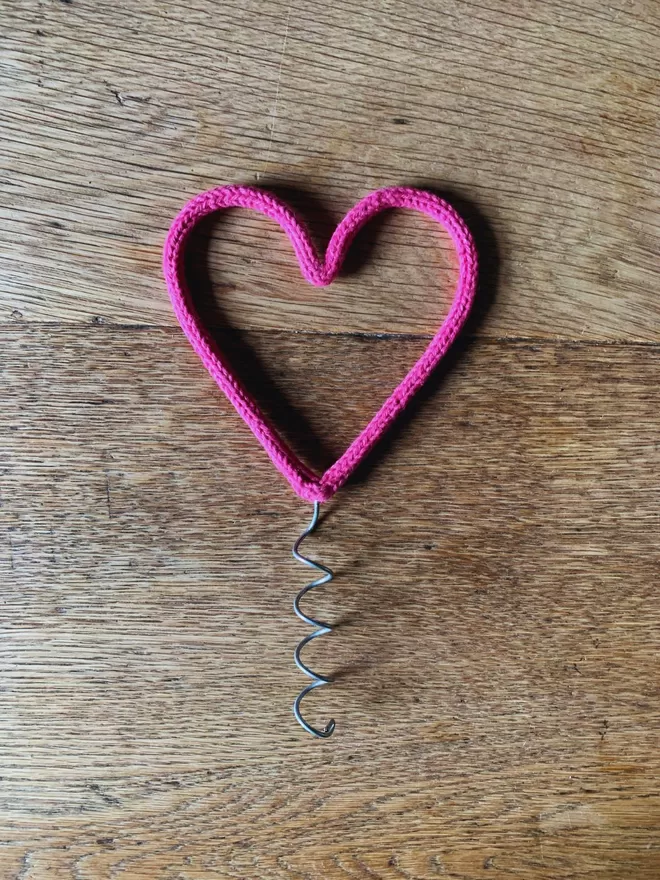 A pink string wrapped wire heart shaped Christmas tree topper on an oak table