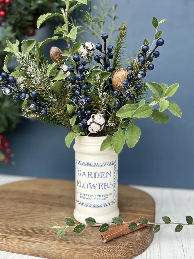 Handmade ceramic jar filled with Christmas foliage. Jar is decorated with a label saying garden flowers