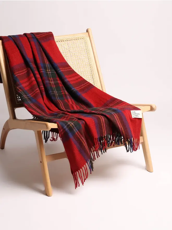 Royal Stewart Blanket, a red blanket draped over a wooden chair on a white surface against a plain backdrop. 