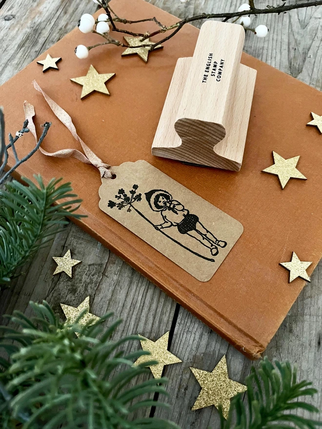 A swing tag showing a Christmas Pixie stamped in black next to a wooden rubber stamp