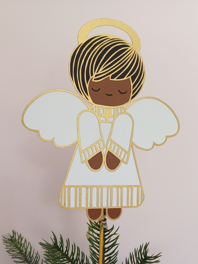 Angel Christmas Tree Topper on Christmas Tree. Angel has black and gold hair, gold halo, wears white and gold tunic and has dark brown skin