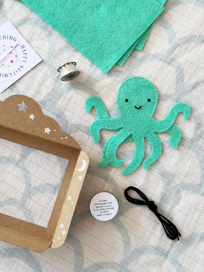 A handmade felt octopus finger puppet lays beside the craft kit components to make it on a fabric surface.