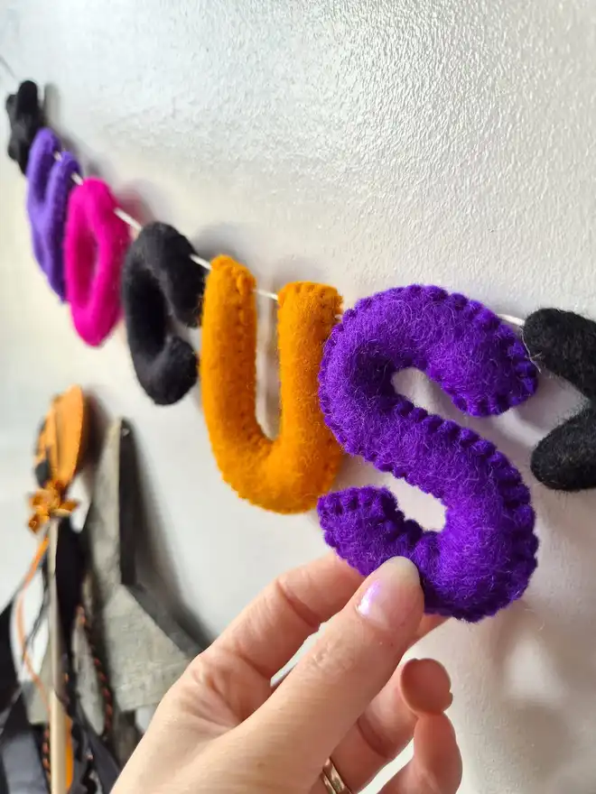 Close up of a felt Halloween garland, featuring the word 'Hocus Pocus' in pink, orange, black and purple