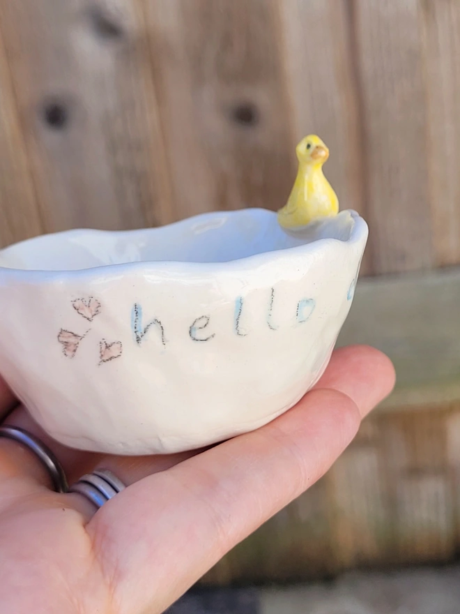 a close up of a cream pottery tealight holder with hearts and hello on the side and a yellow ceramic duck on the rim