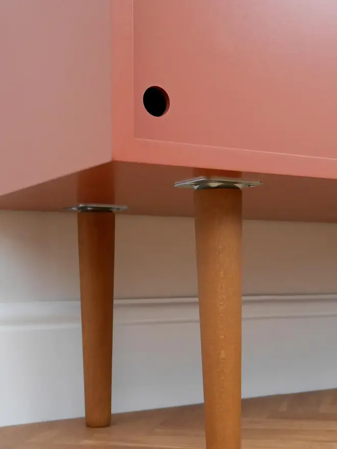 Mid-century cabinet with coral sliding doors and wooden tapered legs.