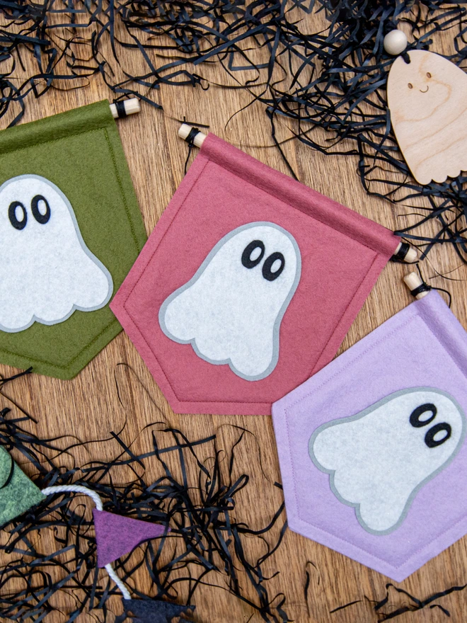 Cute halloween ghost banners made from felt. The white ghost has wide eyes. The banners are shown in 3 different colours, Rose pink, Lilac, and Mossy green.