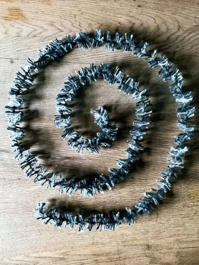 Silver dyed jute string tinsel AKA Strinsel laid out in a spiral on an oak table