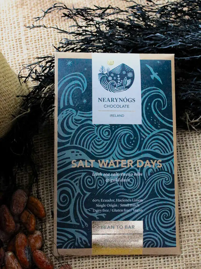 packaged chocolate bar on surface with cacao beans and seaweed