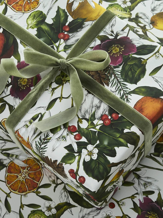 A busy ivory based christmas wrap with festive elements like clementines, holly and hellebores