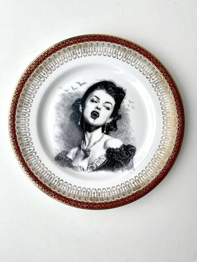 A vampire with bats behind her, the image is victorian in black and white and is printed directly onto an ornate vintage plate