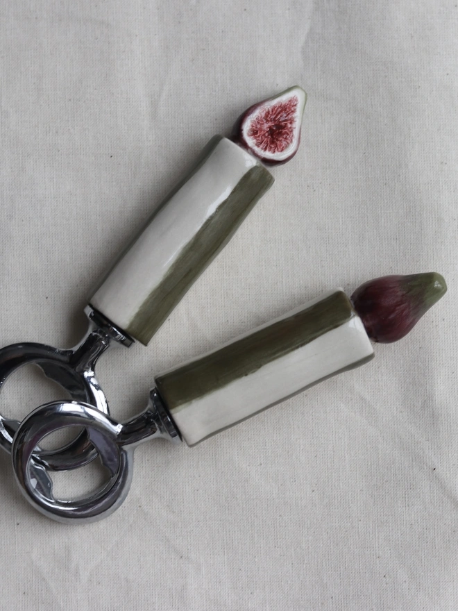 Tube, Olive, Chilli, Or Pickle Bottle Openers, a group of bottle openers on a white tablecloth. They each have a small food or fruit design. 