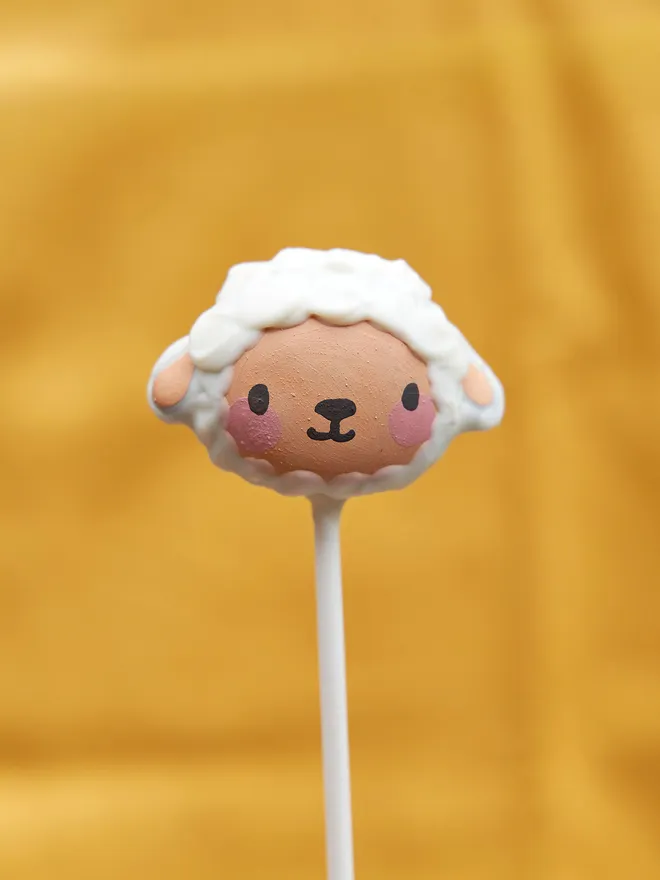 Easter Lamb cake pop held up against a yellow backdrop 
