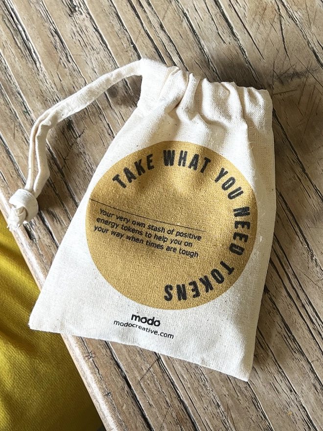 A small drawstring bag with "Take what you need tokens" printed on. The drawstrings are pulled tight. 