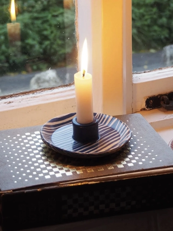 Ceramic Patterned Candlestick Holder, a colourful candlestick holder sitting on a window sill. It is accompanied by a lit candle. 