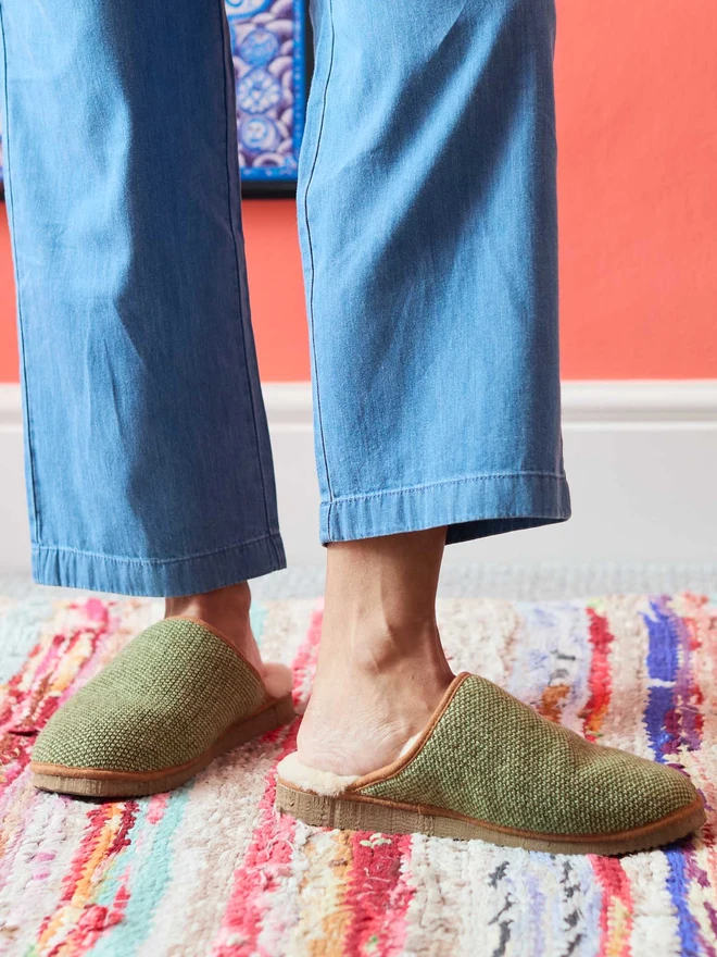 Lambswool & Sheepskin Slippers, a pair of colourful lambswool and sheepskin slippers sitting modelled in front of a colourful wall. 