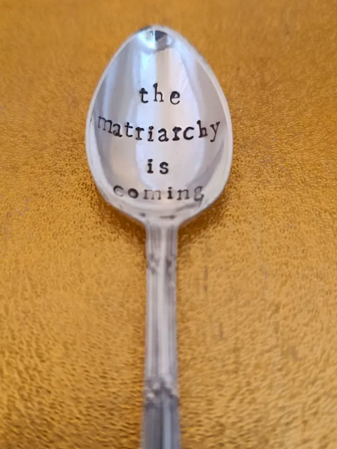 Teaspoon on gold background stamped with the matriarchy is coming 