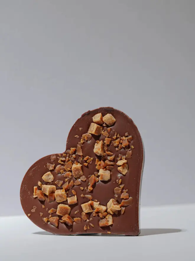 Milk chocolate heart with fudge and toffee pieces on a white background. 