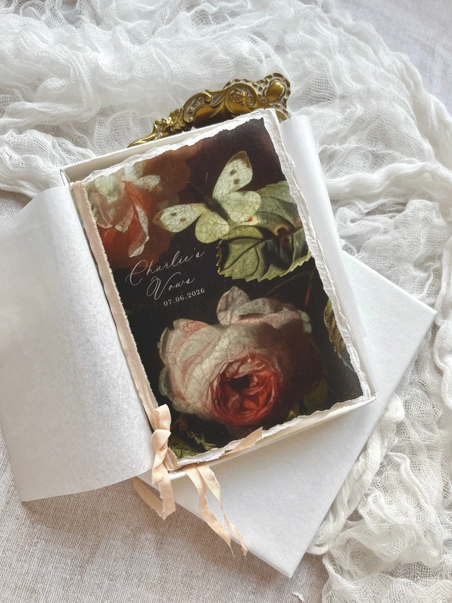 Butterfly and Roses vow booklet. A6 size tied with ribbon. Romantic floral booklet with the design printed on vellum and with 2 handmade paper inserts giving 8 sides on which to write your vows. Shown here with a luxury gift box and tissue paper.