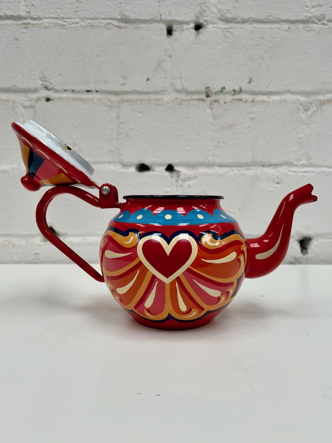 Small red vintage enamel teapot, hand painted with a traditional fairground inspired design in pink, orange and yellow. Teapot has a hinged lid.