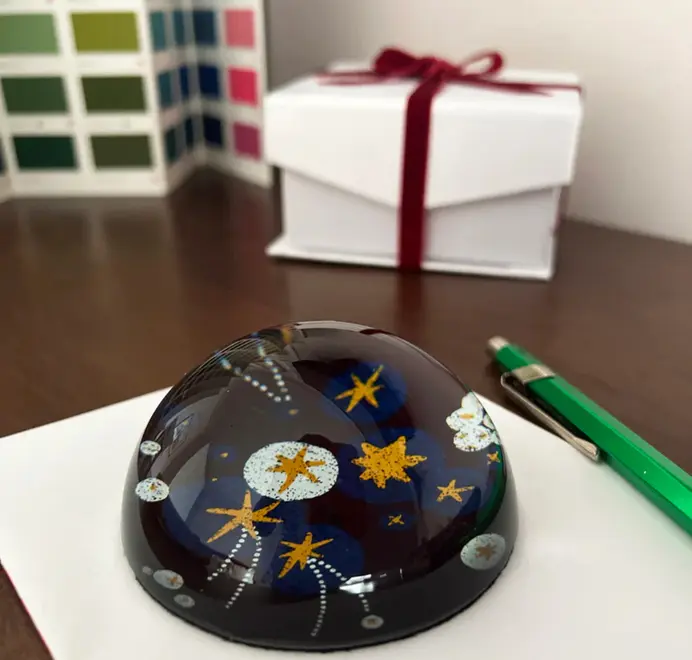 Glossy dome-shaped paperweight with gold stars on a dark blue background on a desk, with a pen and gift box in the background.